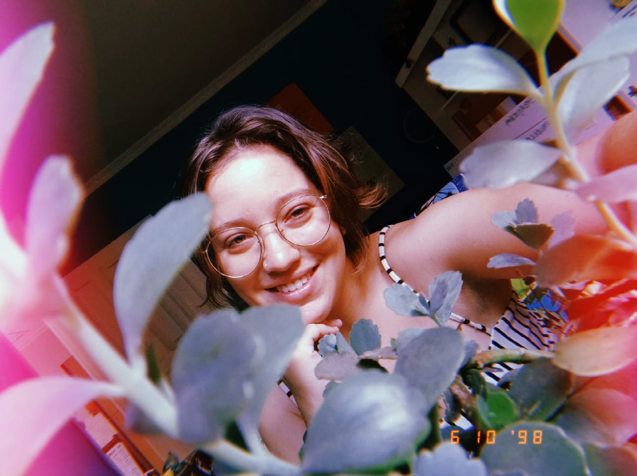 uma foto minha sorrindo, mas a camera tá atrás de um vaso de plantas, então tem várias plantinhas entre a camera e eu, fazendo tipo uma moldura pro meu rosto