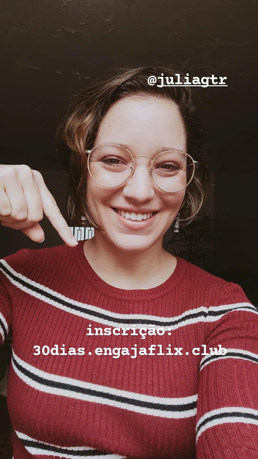 uma foto minha modo selfie usando uma blusinha de lã vermelha com listras pretas e brancas. tô sorrindo e apontando pra um texto que diz: inscrição: 30dias.engajaflix.club. 